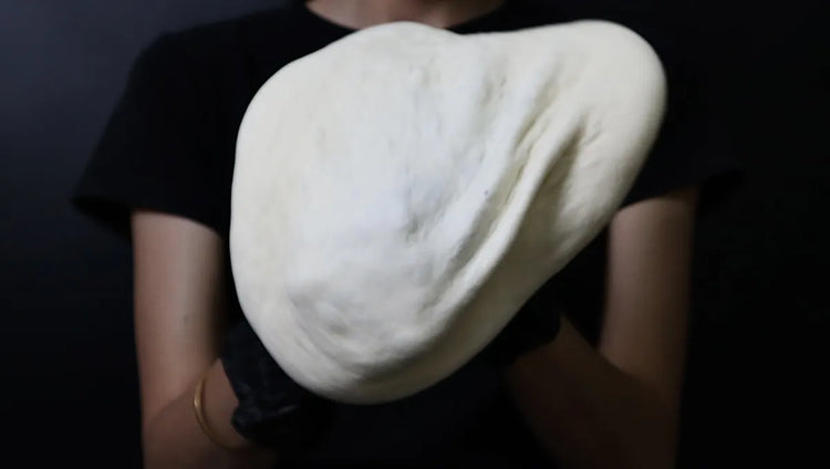 Hands stretching pizza dough over both fists while preserving the raised outer rim