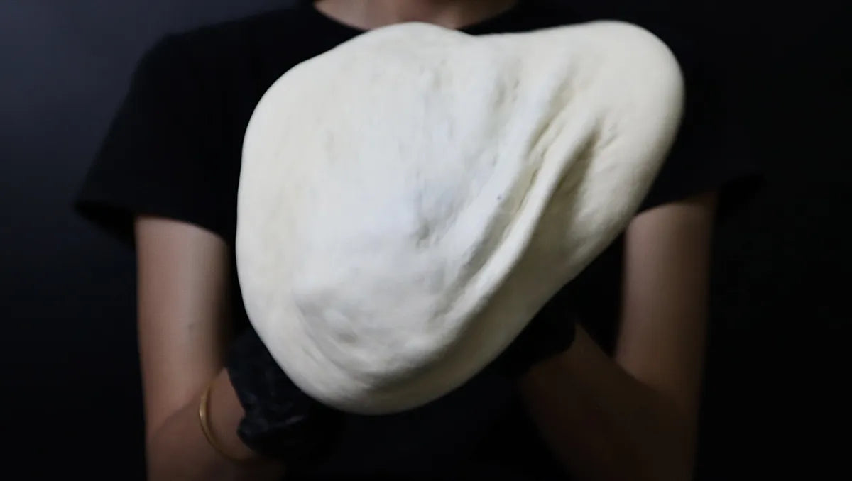Hands stretching pizza dough over both fists while preserving the raised outer rim