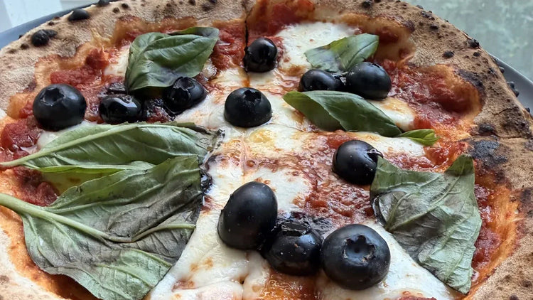 Homemade blueberry Margherita pizza with leopard-spotted Neapolitan crust, mozzarella, basil, and burst blueberries