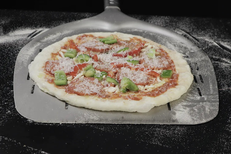 Topped pizza moving freely on a perforated metal peel dusted lightly with semolina