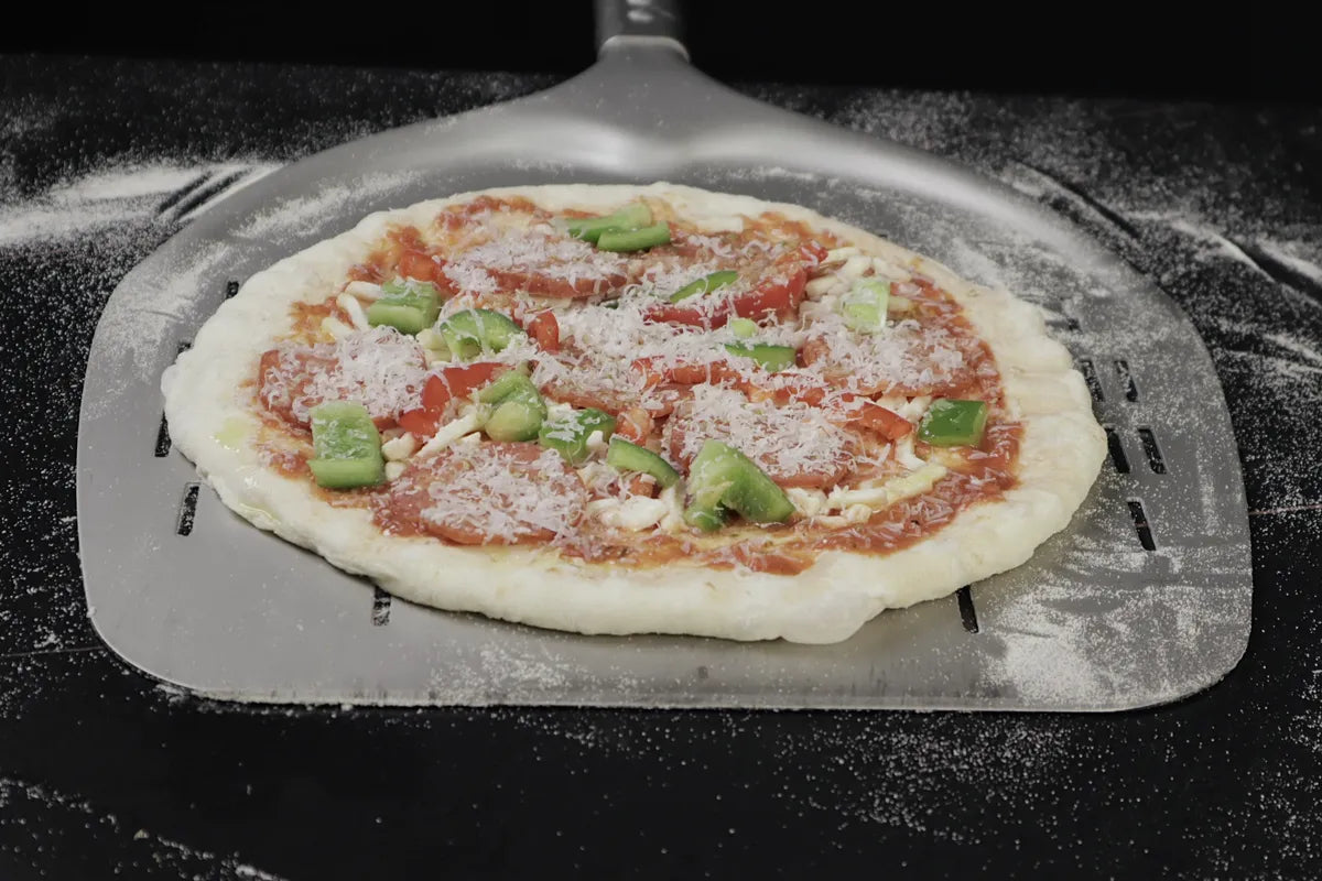 Topped pizza moving freely on a perforated metal peel dusted lightly with semolina