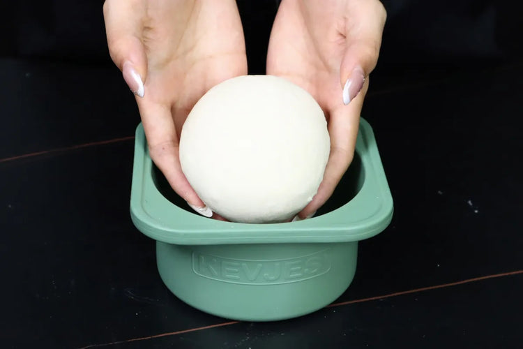  Hands placing a smooth 230 gram pizza dough ball into a green KEVJES Classic proofing container